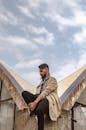 Fashionable young man with a full beard sitting on a modern urban structure outdoors.